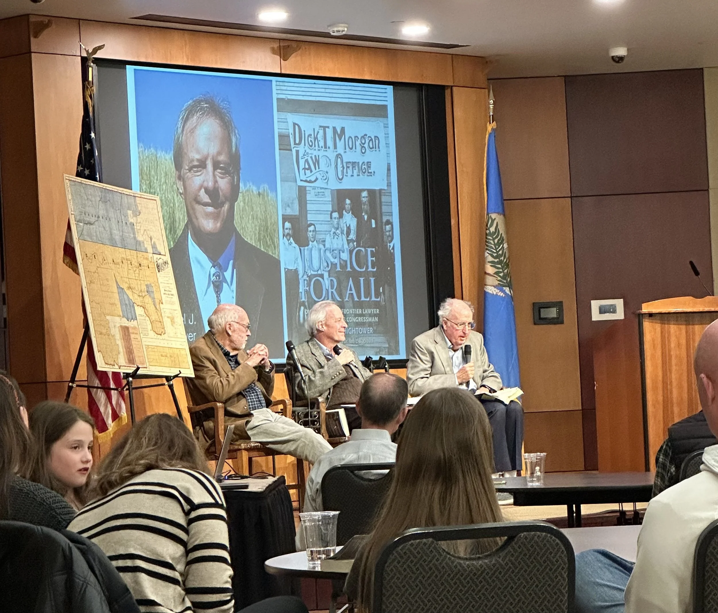 anel discussion at the Oklahoma History Center on February 26, 2025, with three men seated on stage and a projected image of the Justice for All book cover behind them