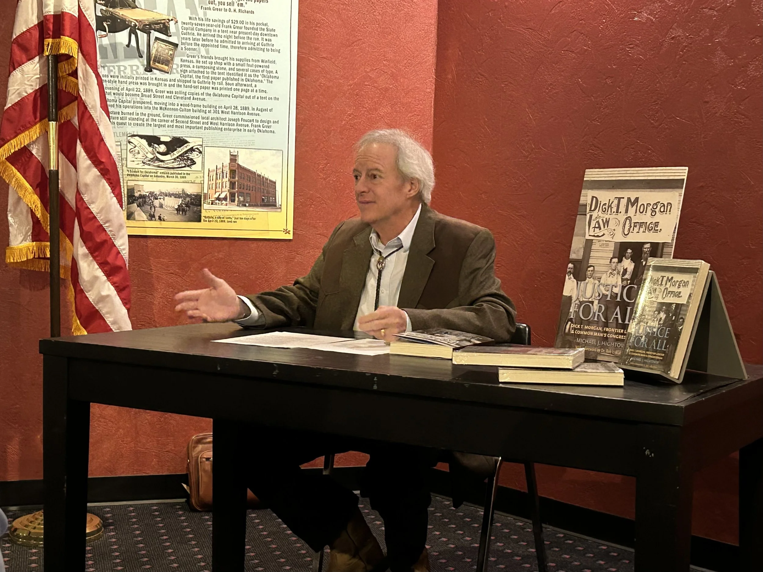 Michael J. Hightower speaking at a table during a presentation at the Oklahoma Territorial Museum on February 21, 2025, with the Justice for All book displayed beside him